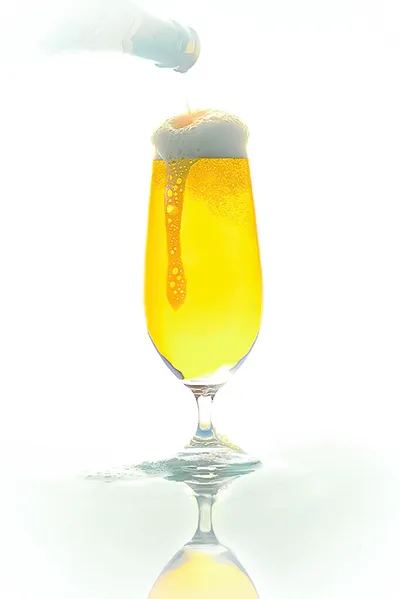 Biergläser & Bierkultur – Perfekter Genuss für Kenner Dynamische Getränkefotografie: Ein hohes, schlankes Bierglas, das von oben mit einem goldgelben Bier aus einer Flasche gefüllt wird. Eine dicke, cremige Schaumkrone bildet sich, und etwas Schaum läuft am Glas herunter. Der Hintergrund ist hell und reinweiß.